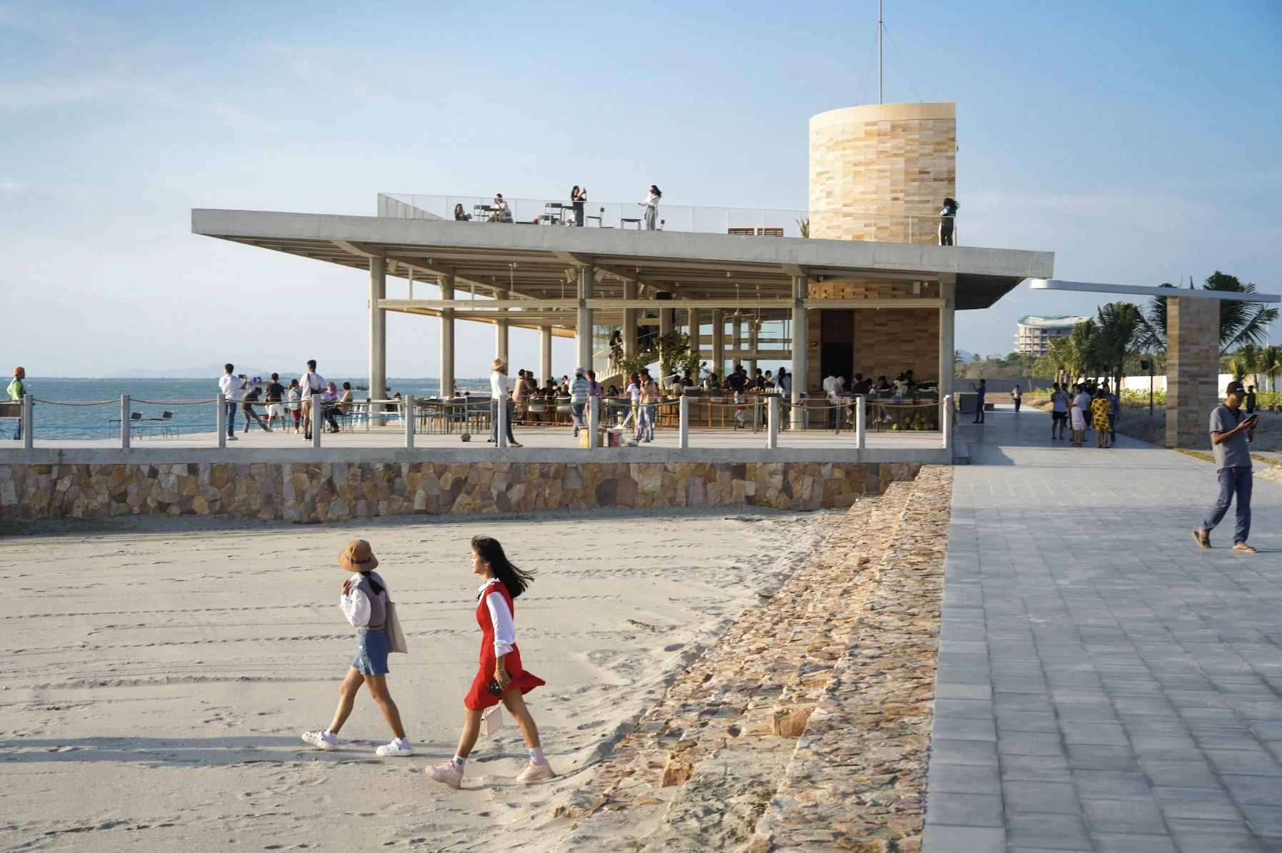 Visitors on the beach and promenade by the seafront pavilion at Kep West